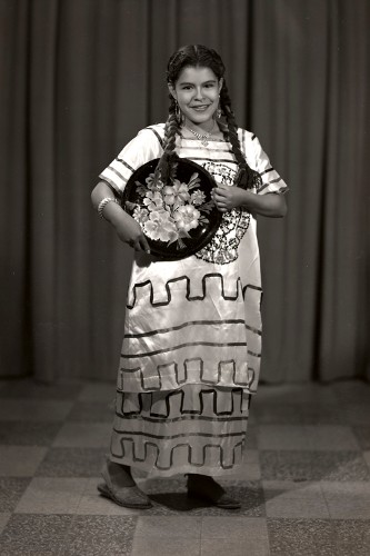 Imagen de Retrato de niña con vestido de manta bordado y charola con motivos vegetales, probablemente después de un baile escolar, en estudio (atribuido)