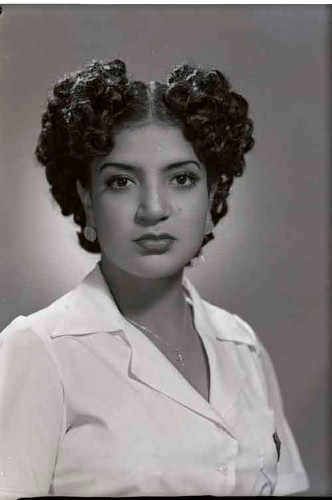 Imagen de Retrato de mujer joven con vestido formal, peinado estilizado, aretes con silueta clásica y crucifijo en pecho en estudio (atribuido)