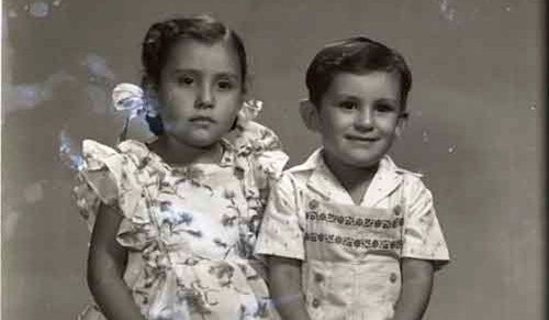 Imagen de Retrato de niña y niño hermanitos sentados con ropa formal con estampados y botas en estudio (atribuido)