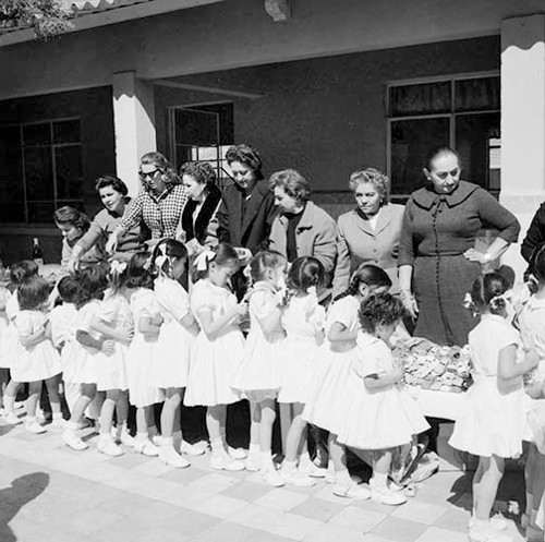 Imagen de Niñas recibiendo dulces y chocolates de damas elegantes durante la celebración del día del niño en una escuela (propio)